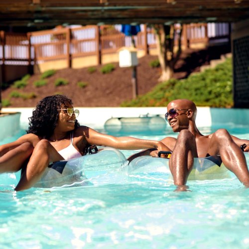 Two people relax in inner tubes on a sunny day at a pool, enjoying the water and each other's company.
