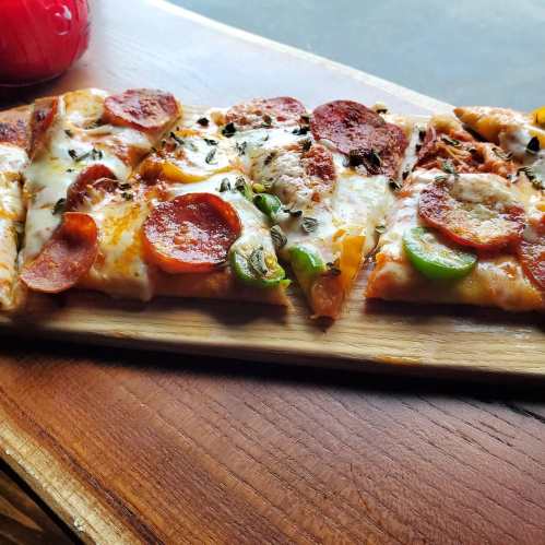 A wooden platter with slices of pepperoni pizza topped with green peppers and herbs.