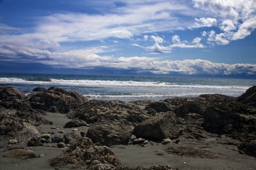 A rocky beach with waves crashing against the shore under a partly cloudy sky.