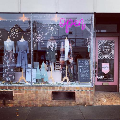 A boutique storefront with a neon "open" sign, displaying winter clothing and festive decorations in the window.