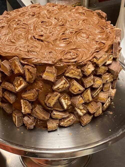 A large chocolate cake decorated with swirls of frosting and surrounded by pieces of chocolate candy.