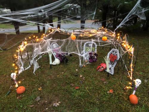 A spooky Halloween display with cobwebs, lights, tombstones, and decorations in a grassy area.