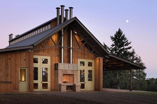 A modern wooden house with large windows, a stone fireplace, and a metal roof, set against a twilight sky.
