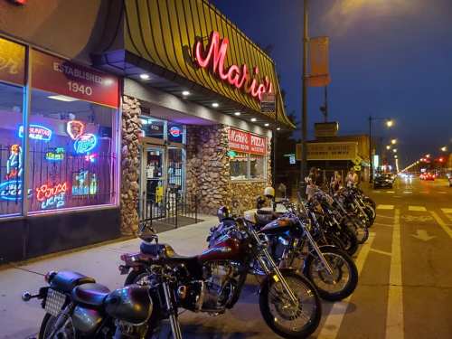 A nighttime view of Mario's restaurant with neon signs and parked motorcycles outside.