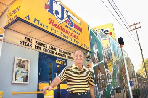 A smiling man stands in front of a colorful restaurant with a sign that reads "RJ's Restaurant - A Place For Family Fun & Food."