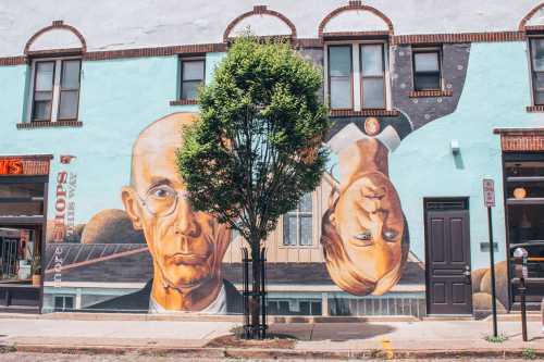A mural featuring two portraits, one of a man and one of a woman, on a colorful wall with a tree in front.