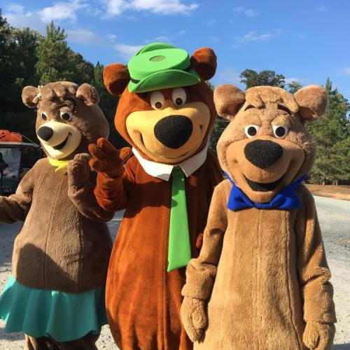Three cartoon bear characters in costumes, smiling and posing outdoors among trees.