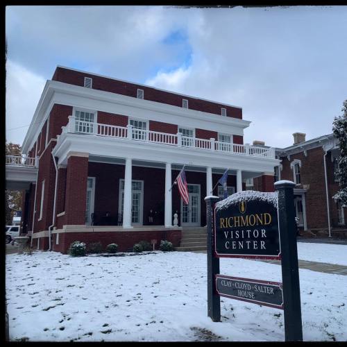 Historic Richmond Visitor Center, a red brick building with white columns, surrounded by light snow and flags.