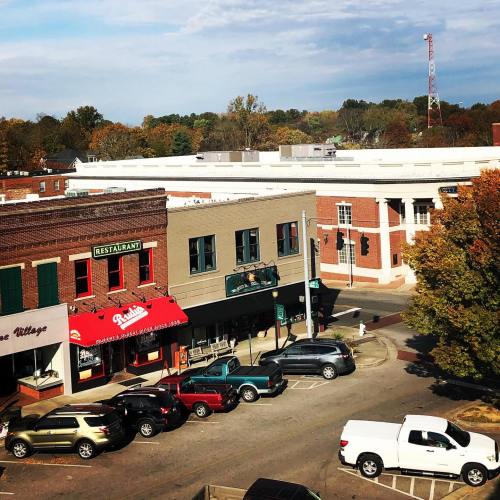A view of a small town street with shops, parked cars, and autumn trees under a partly cloudy sky.