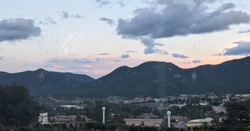 A scenic view of mountains at sunset, with clouds and a small town visible in the foreground.