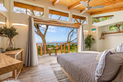 Bright bedroom with large windows overlooking a scenic view, featuring wooden accents and a cozy atmosphere.