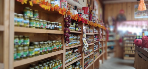 A cozy store interior with shelves lined with jars of pickles and preserves, decorated with autumn leaves.
