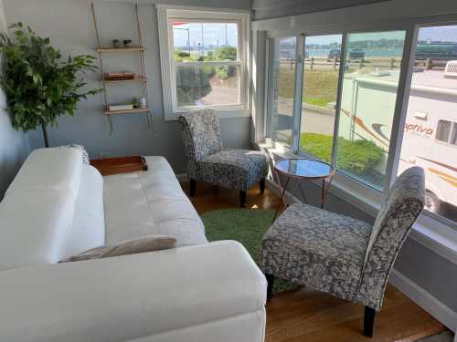 Cozy living space with a white sofa, patterned chairs, and large windows overlooking a scenic view.