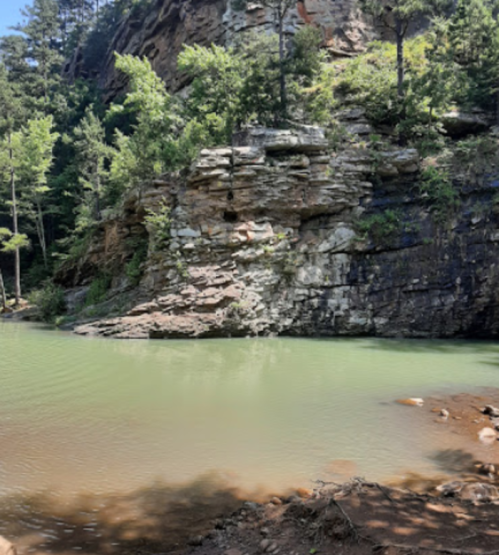 A serene riverbank with rocky cliffs and lush greenery under a clear blue sky.