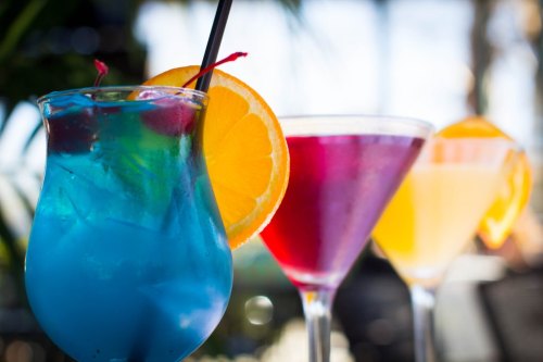 Three colorful cocktails with garnishes of orange slices and cherries, set against a blurred background.