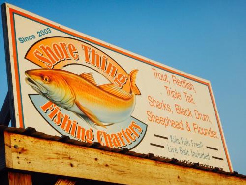 Sign for "Shore Thing Fishing Charters" featuring a large fish and listing various fish species available for catch.