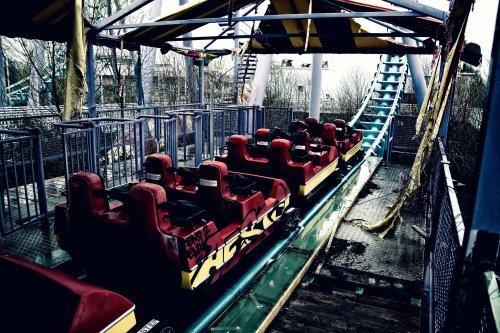 Abandoned roller coaster with empty seats, overgrown surroundings, and a gloomy atmosphere.
