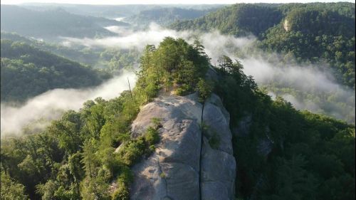 Aerial view of a rocky ridge surrounded by lush green hills and misty valleys.