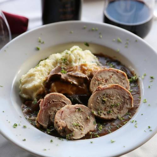 A plate of sliced meat rolls served with mashed potatoes and gravy, garnished with herbs.