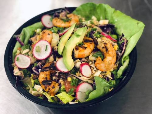 A vibrant salad topped with grilled shrimp, avocado, radishes, and mixed greens in a black bowl.