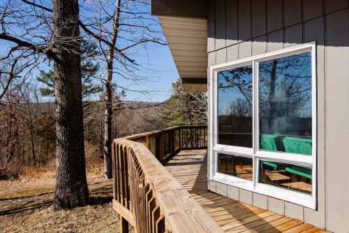 A wooden deck wraps around a modern house, surrounded by trees and a scenic view of the landscape.