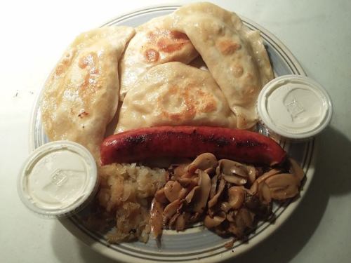 A plate with fried dumplings, a grilled sausage, sautéed mushrooms, and two containers of sauce.