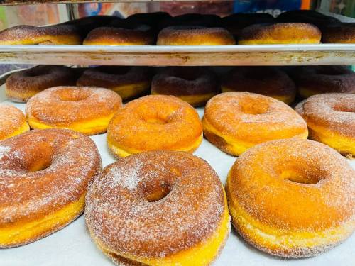 A close-up of freshly baked donuts, golden brown and dusted with sugar, arranged on a tray.