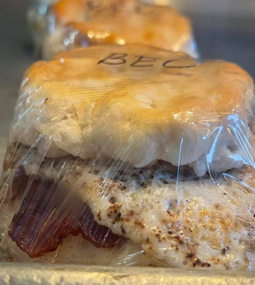 A close-up of a wrapped biscuit sandwich with bacon and egg, labeled "BEC."
