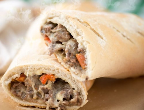A close-up of a stuffed sandwich, revealing savory beef, peppers, and melted cheese inside a soft bread roll.