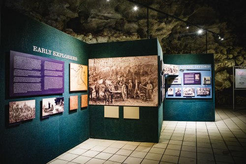Exhibit showcasing early explorers with informational panels and historical photographs in a cave-like setting.