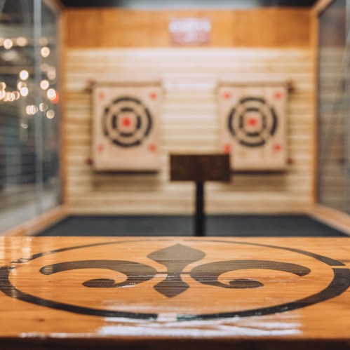 A wooden table with a decorative design in the foreground, with two target boards in the background for axe throwing.
