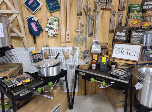 Display of cooking equipment and accessories, including pots, utensils, and decorative items, in a rustic wooden setting.