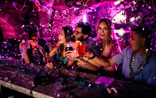 A group of friends celebrating at a party, raising drinks amidst colorful confetti and festive decorations.