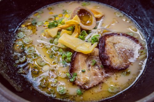 A bowl of ramen with rich broth, sliced pork, green onions, bamboo shoots, and a soft-boiled egg.