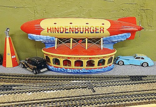 A colorful model of a zeppelin labeled "HINDENBURGER" next to toy cars and a train track on a textured surface.