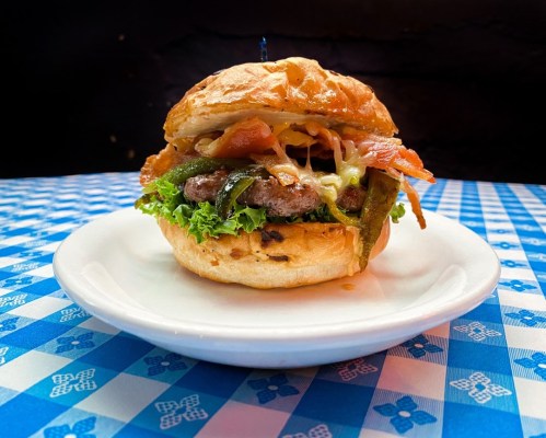 A delicious burger with lettuce, bacon, cheese, and jalapeños on a toasted bun, served on a white plate.