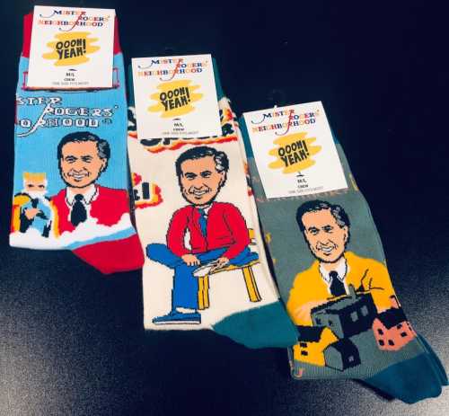 Three pairs of colorful socks featuring Mr. Rogers in various poses, with playful designs and labels.