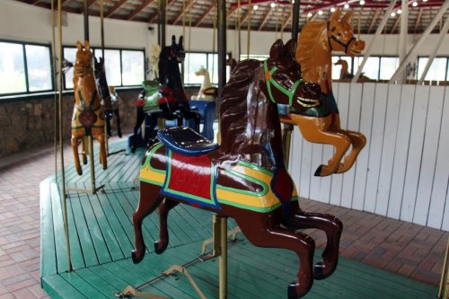 A colorful carousel with painted horse figures, set in a bright indoor space.