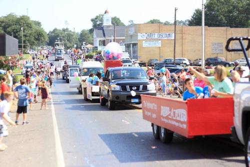 A lively parade with colorful floats and people celebrating along the street, surrounded by spectators.
