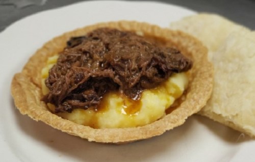 A savory pie filled with mashed potatoes and topped with shredded beef in gravy, served with a side of bread.