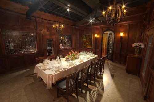 Elegant dining room with a long table set for a meal, surrounded by wooden walls and soft lighting.