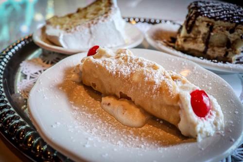 A plate with a cannoli topped with powdered sugar and cherries, alongside slices of cake on a decorative tray.