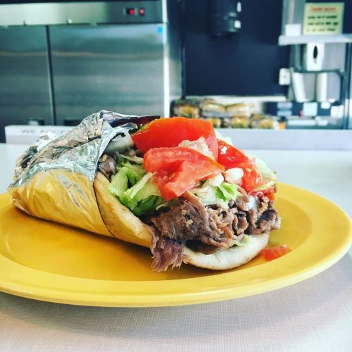 A delicious sandwich filled with shredded beef, lettuce, and tomatoes, served on a yellow plate.