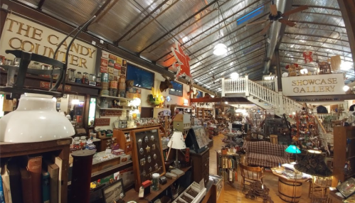 A spacious antique shop filled with vintage items, candy displays, and decorative lights under a metal roof.
