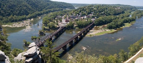 Aerial view of a river winding through green hills, with a town and a bridge crossing the water below.