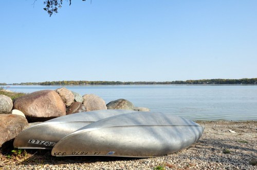 Two silver canoes resting on a rocky shore by a calm lake under a clear blue sky.