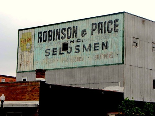 Faded vintage sign for Robinson & Price, seed merchants, on a weathered building.