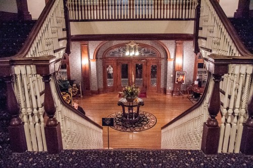 A grand staircase leads to an elegant foyer with a floral arrangement and vintage decor in a historic building.