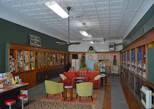 Cozy interior of a library with wooden shelves, a red couch, green chairs, and colorful wall art.