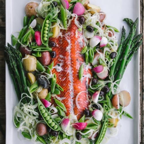 A vibrant platter featuring roasted salmon surrounded by colorful vegetables like asparagus, potatoes, and radishes.